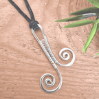 Silver wire-wrapped pendant on a wooden surface with a plant in the corner