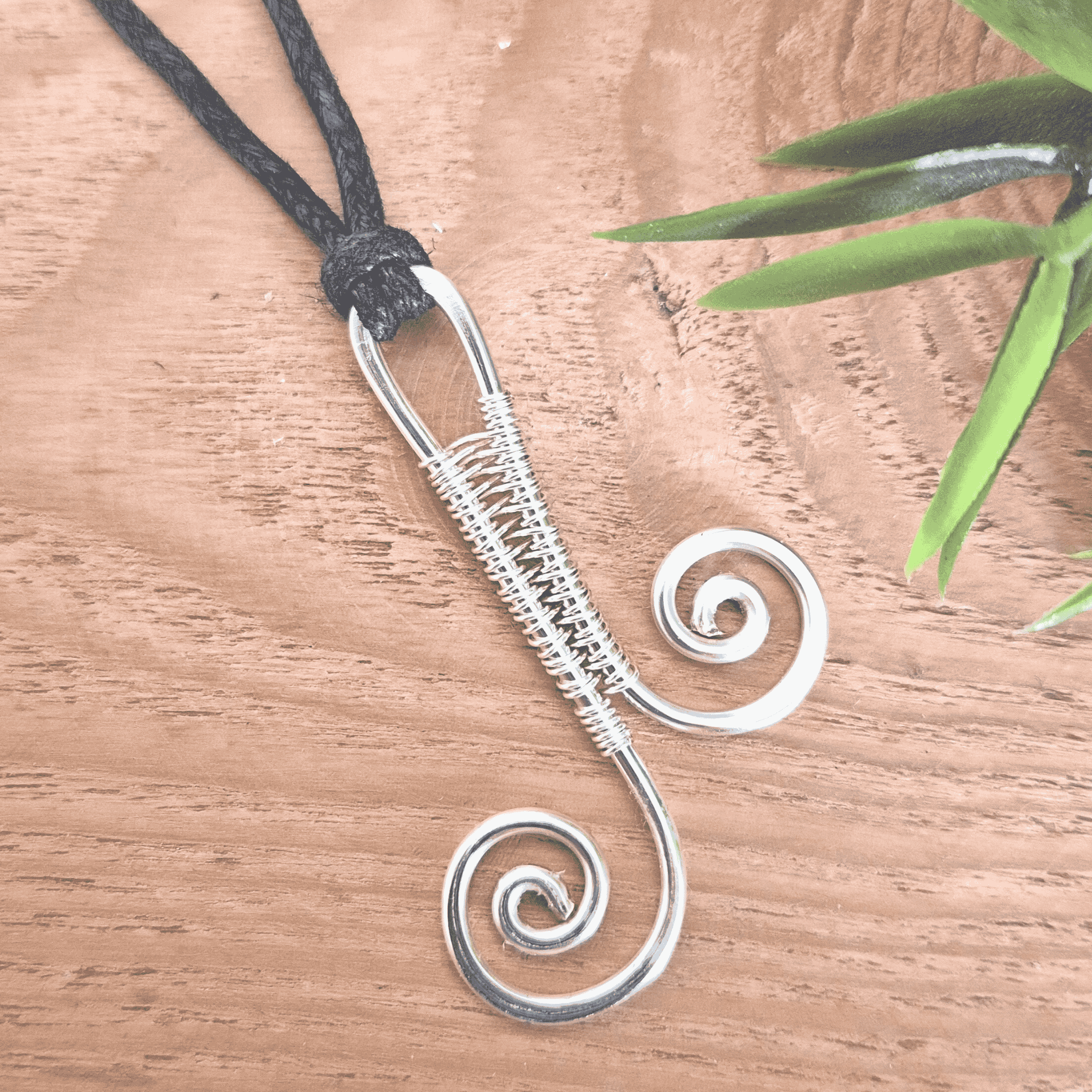 Silver wire-wrapped pendant on a wooden surface with a plant in the corner