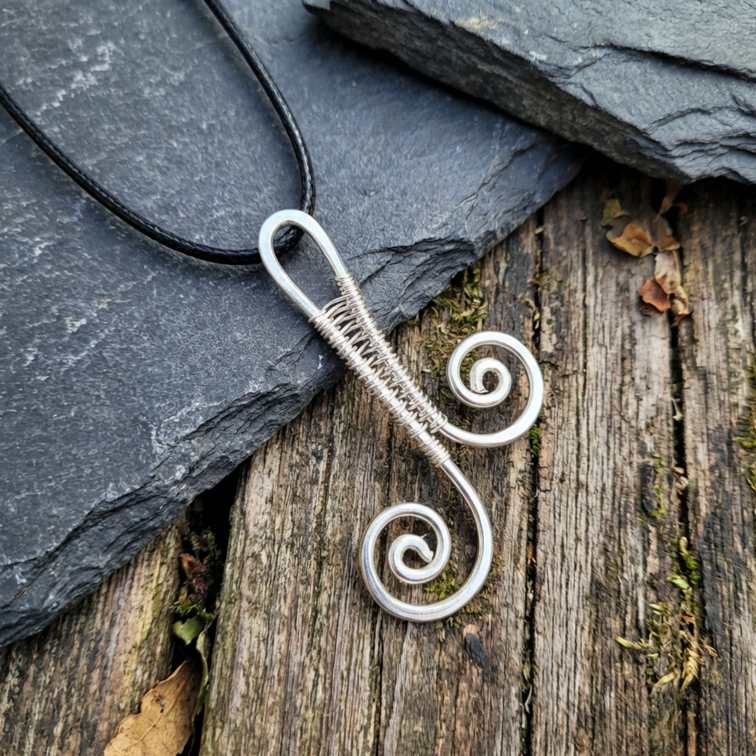 Silver wire-wrapped pendant on a wooden surface with slate stone
