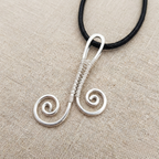 Silver wire-wrapped pendant on a black cord against a beige fabric background