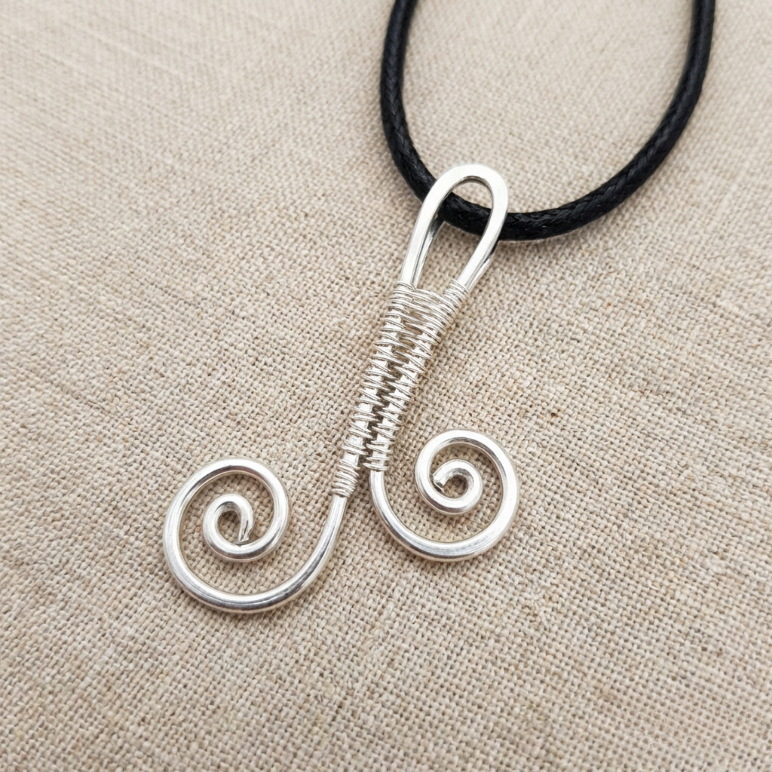Silver wire-wrapped pendant on a black cord against a beige fabric background