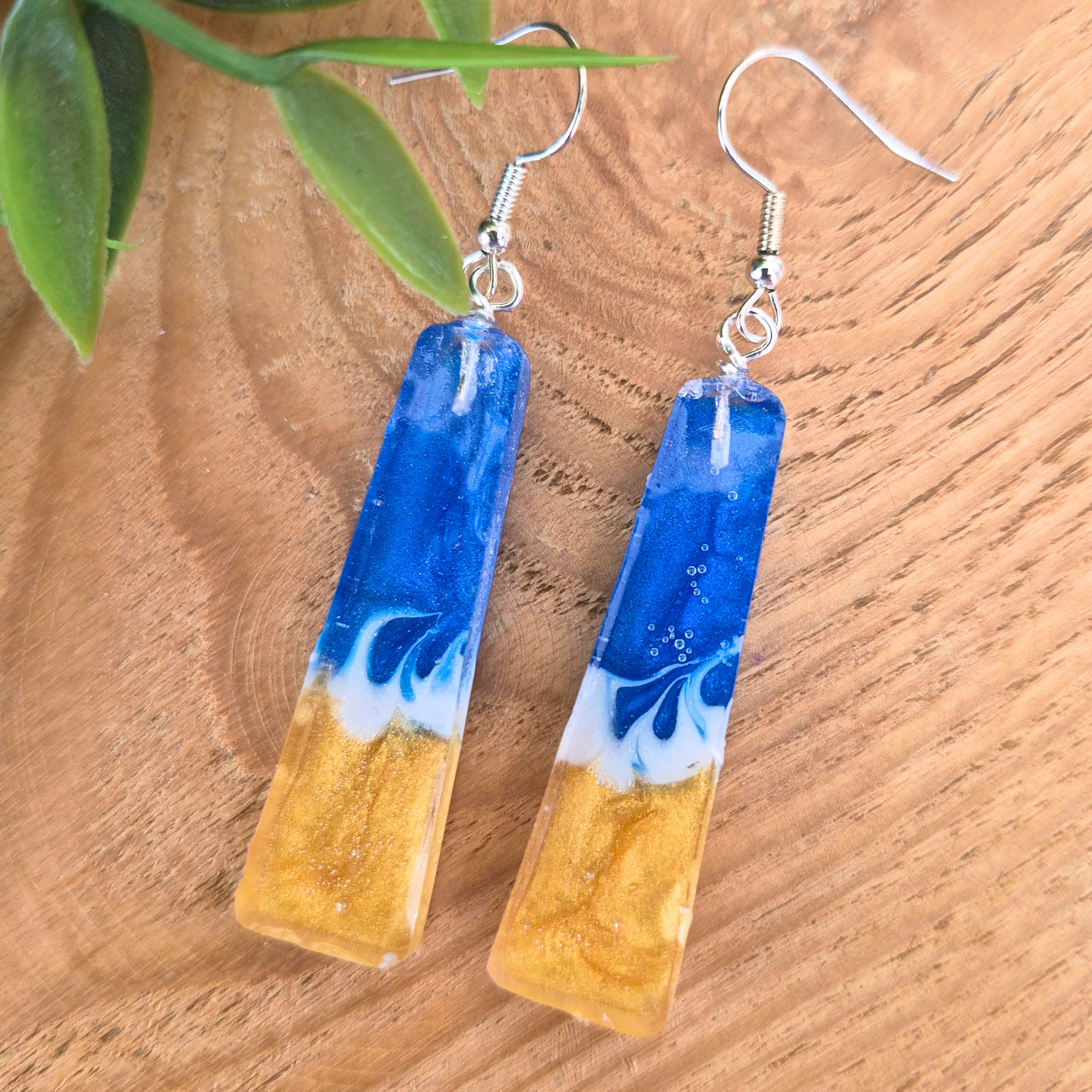 Blue and gold earrings on a wooden surface with a plant leaf in the background
