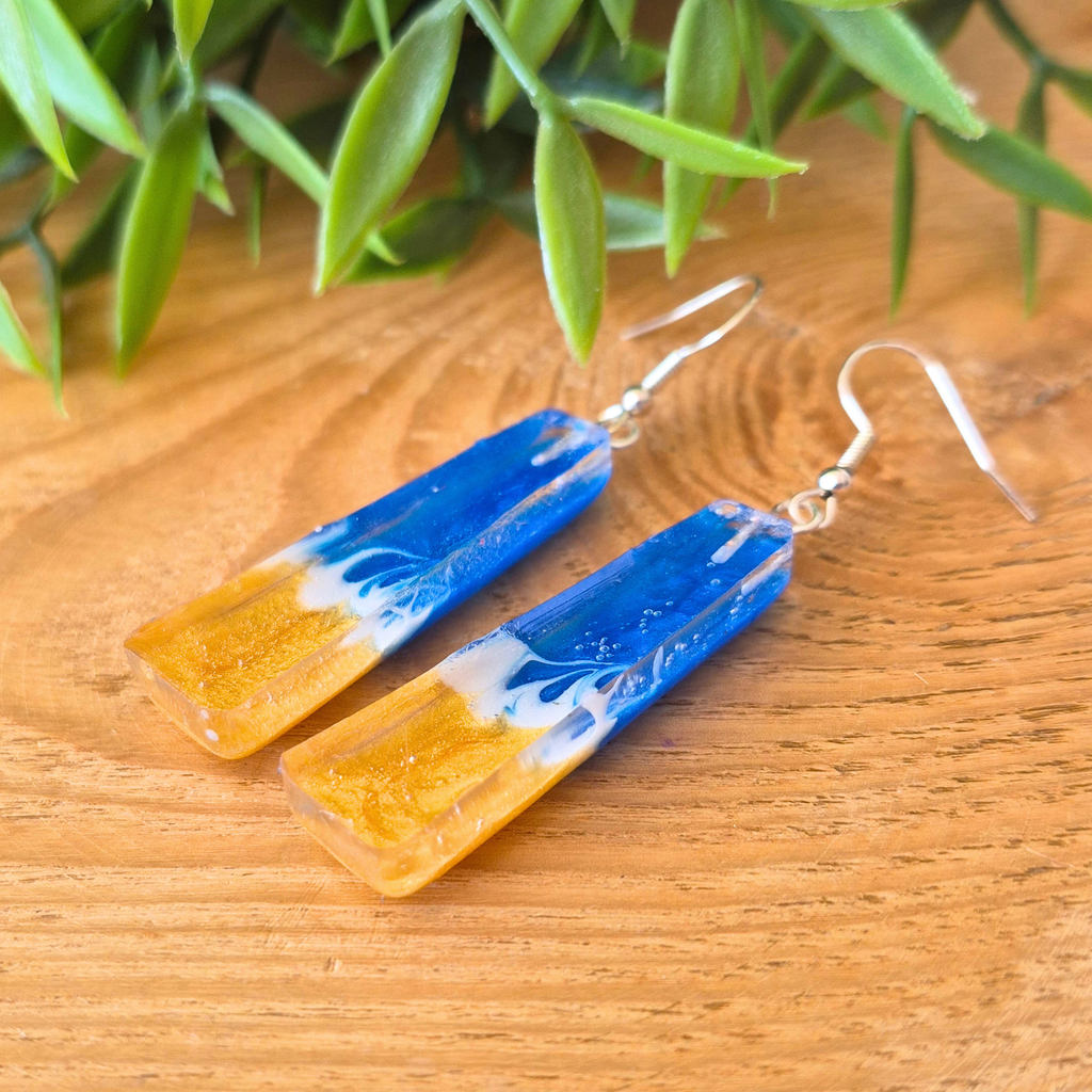 Blue and gold earrings on a wooden surface with green leaves in the background