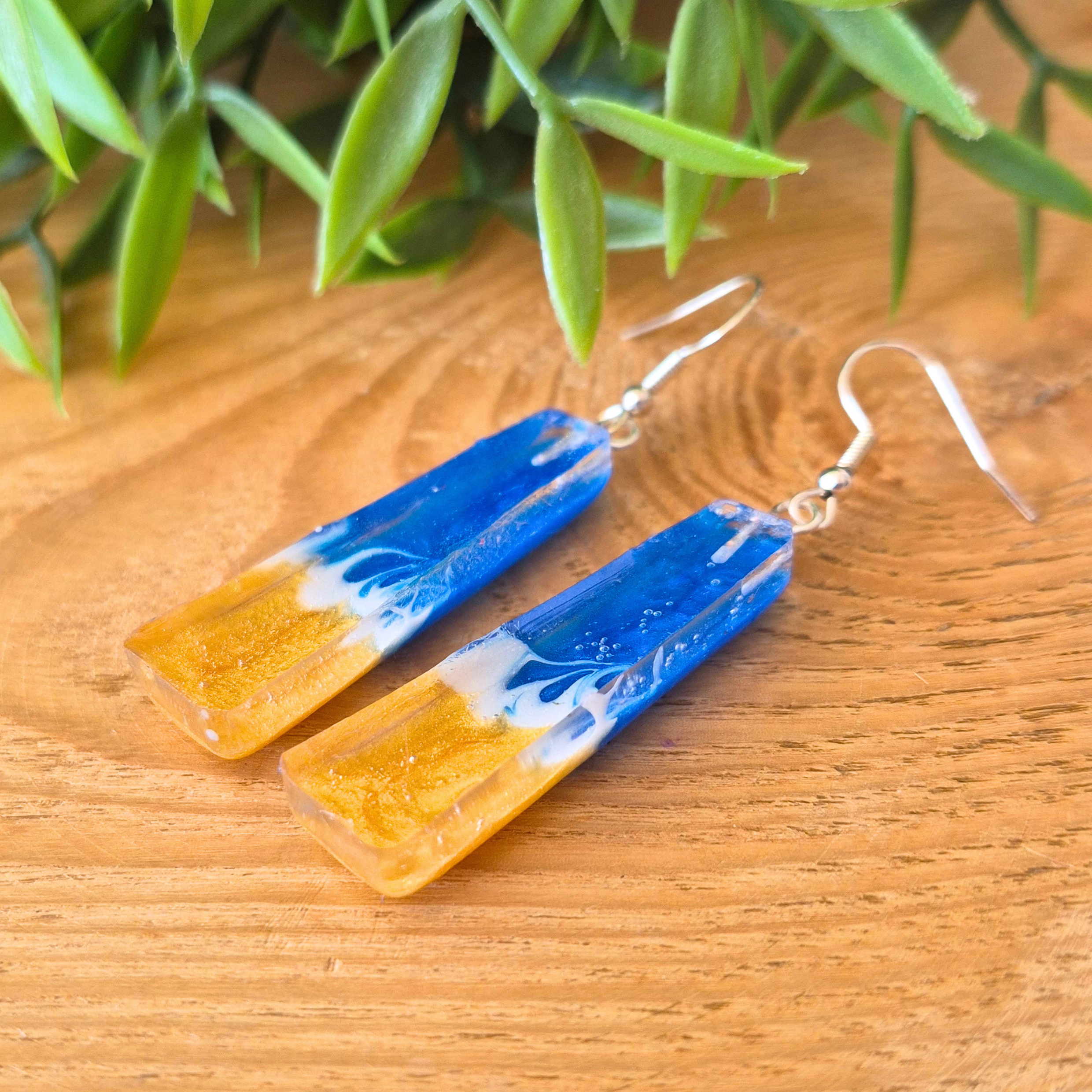 Blue and gold earrings on a wooden surface with green leaves in the background