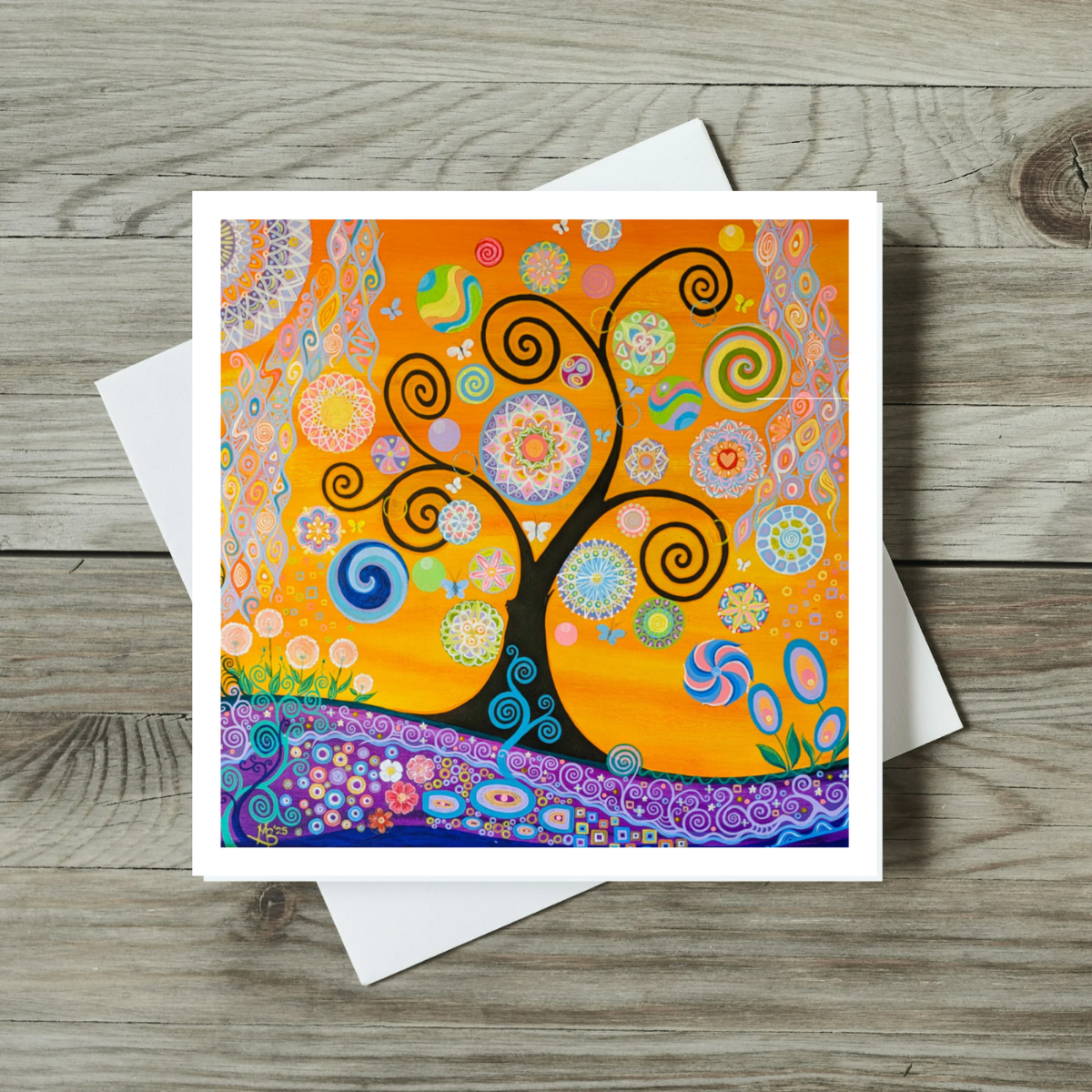 Colourful spiral tree design on a greeting card with a white envelope on a wooden surface