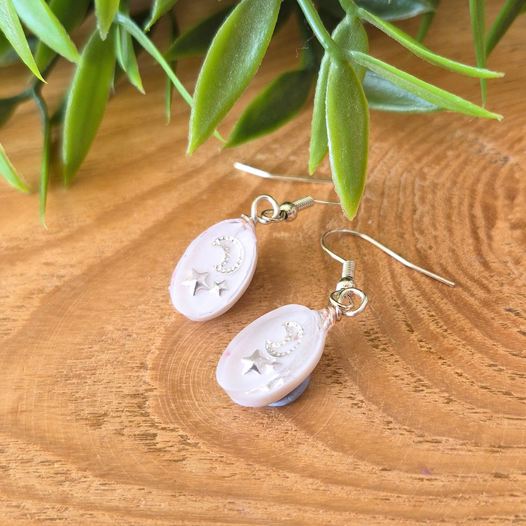 Pair of earrings on a wooden surface with green leaves in the background
