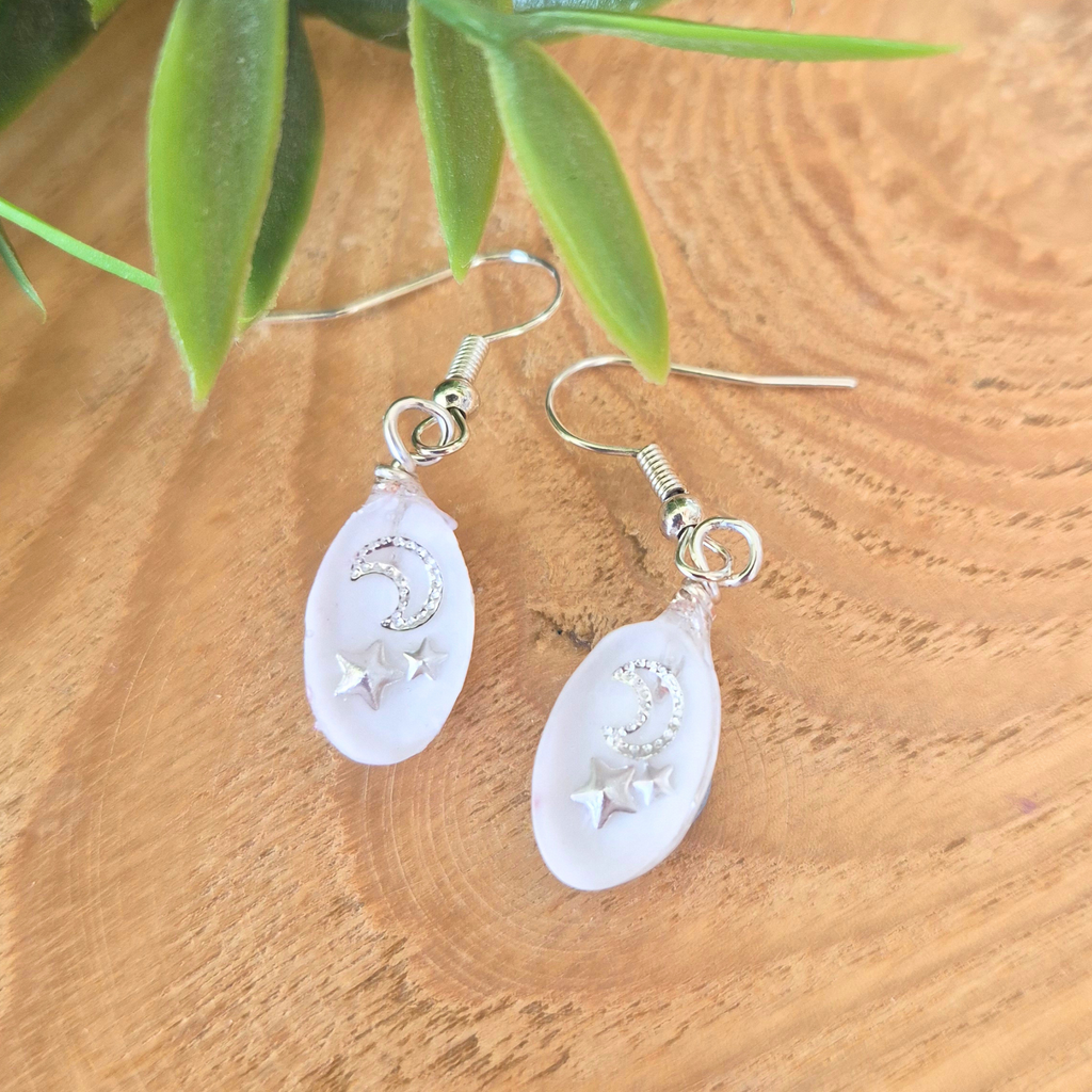 Pair of earrings with moon and star designs on a wooden surface