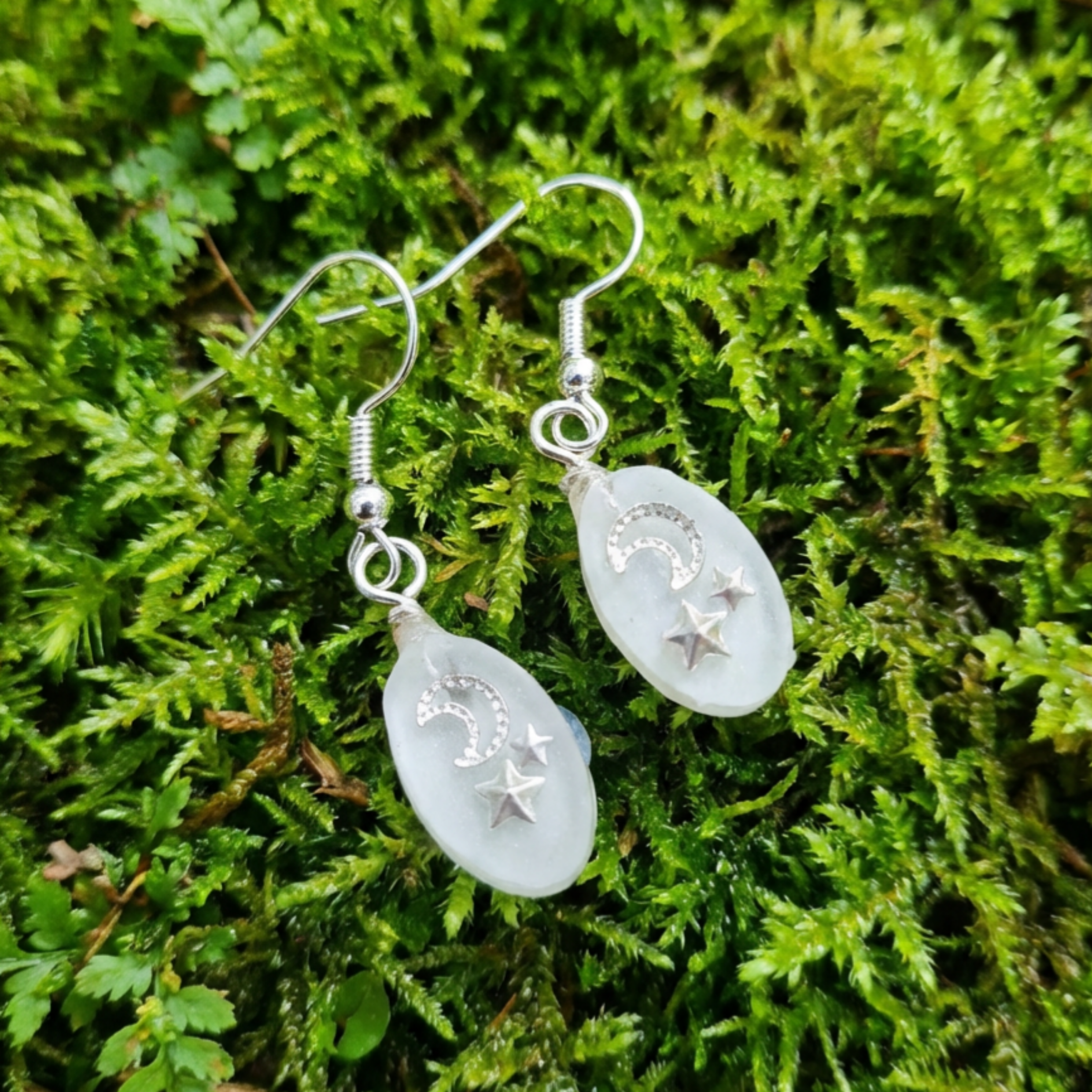 Teardrop-shaped earrings with star designs on a green moss background