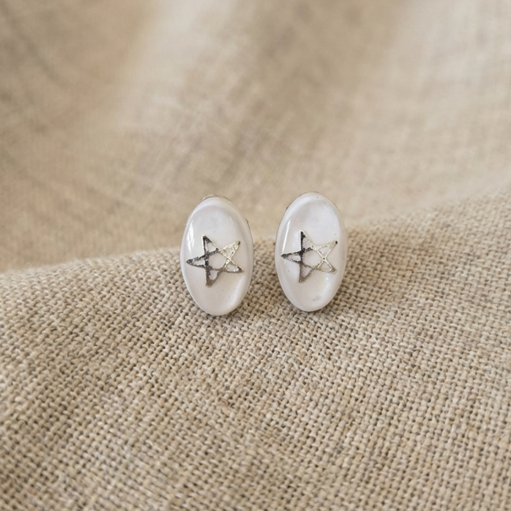 White and clear stud earrings with silver stars on a fabric surface