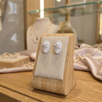 Pair of earrings on a wooden display stand with a blurred jewelry store background.