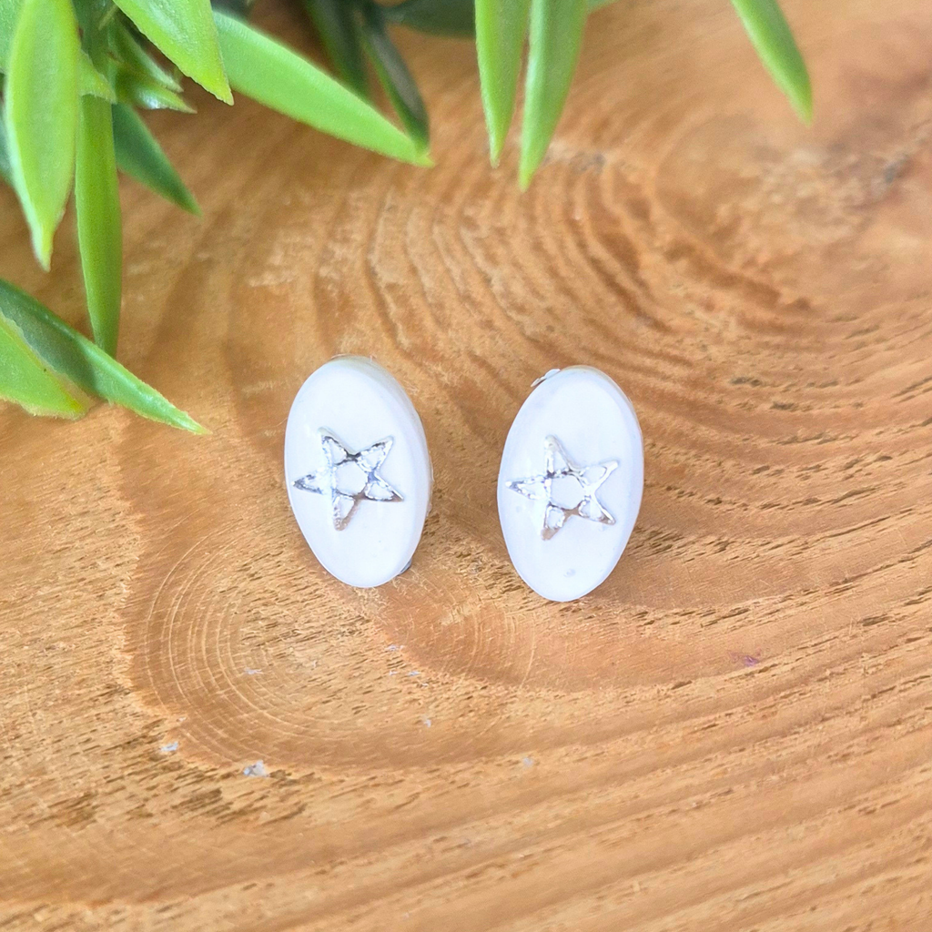 Simple white and clear earrings with silver stars on a wooden surface