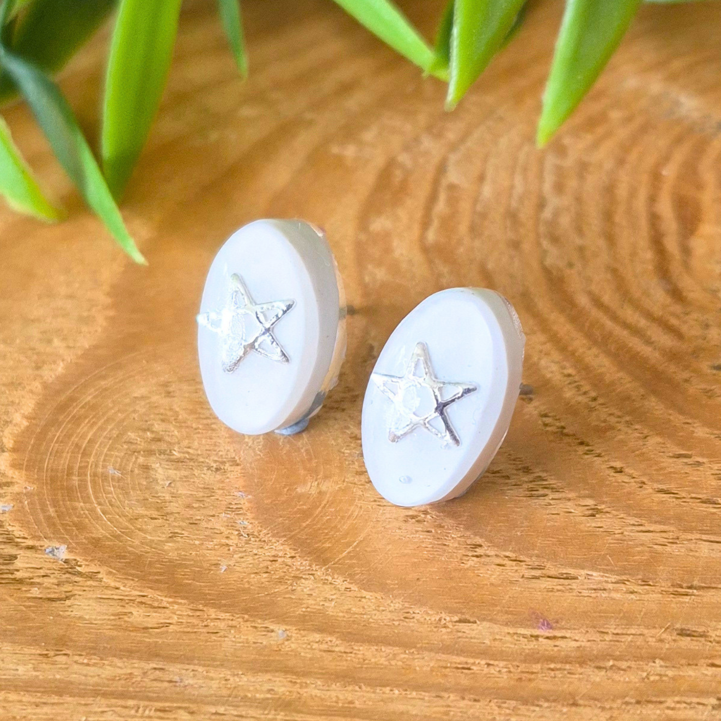 Pair of star-shaped earrings on a wooden surface with green leaves in the background