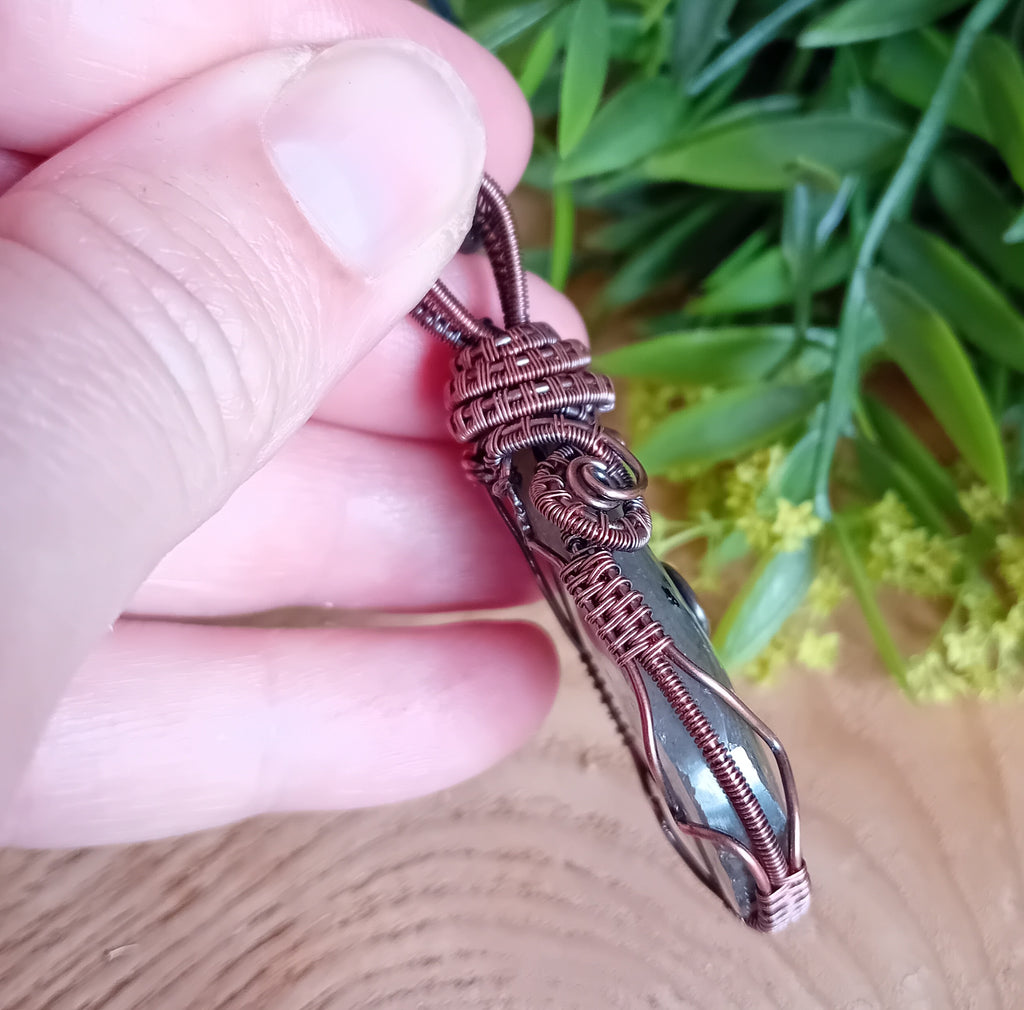 Hand holding a intricately designed copper pendant against a natural background