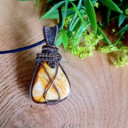 Wire-wrapped pendant with a natural  yellow picture Jasper stone on a wooden surface with greenery