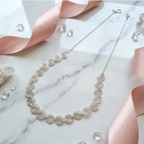 Silver necklace on a marble surface with pink ribbons and crystals