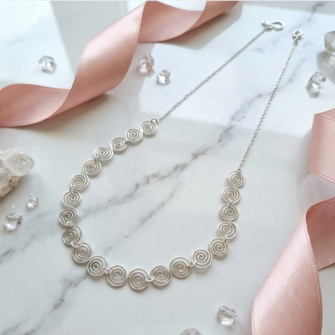 Silver necklace on a marble surface with pink ribbons and crystals
