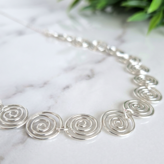 Very close view of the Celtic spirals in this silver spiral necklace on a marble surface