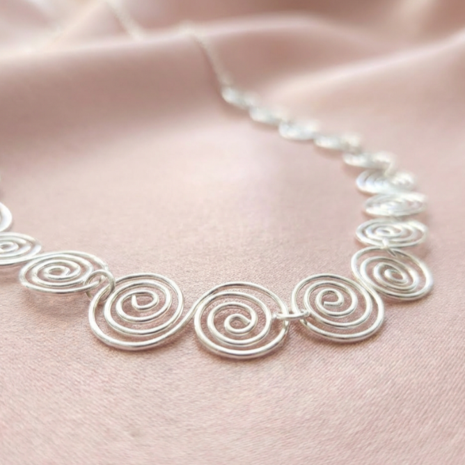 Detailed view of Celtic silver spirals on a pink fabric background