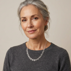 Woman wearing a dark gray sweater and a silver spiral necklace against a beige background