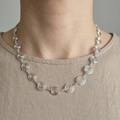 Silver necklace with circular design worn by a person on a plain background
