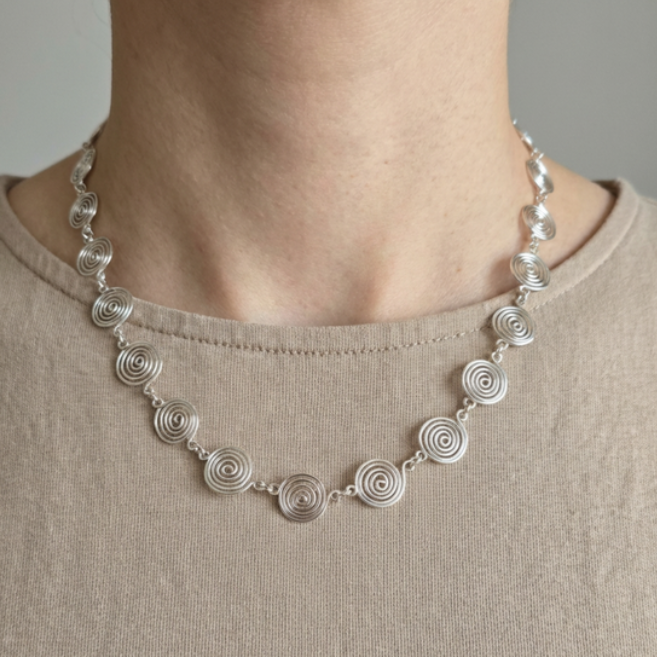 Silver necklace with circular design worn by a person on a plain background