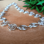 Silver spiral necklace on a wooden surface with green leaves in the background