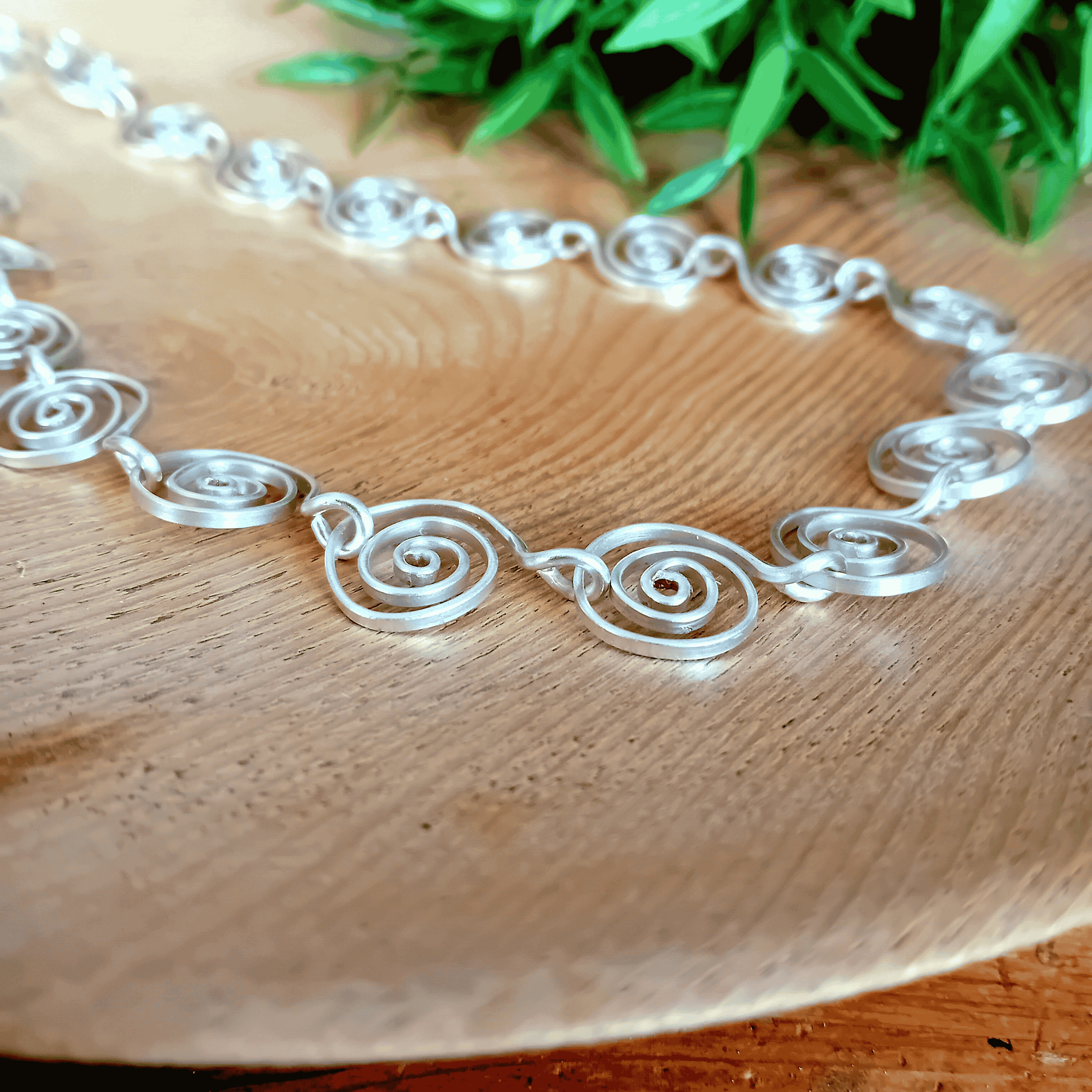 Alice Silver spiral necklace on a wooden surface with green leaves in the background