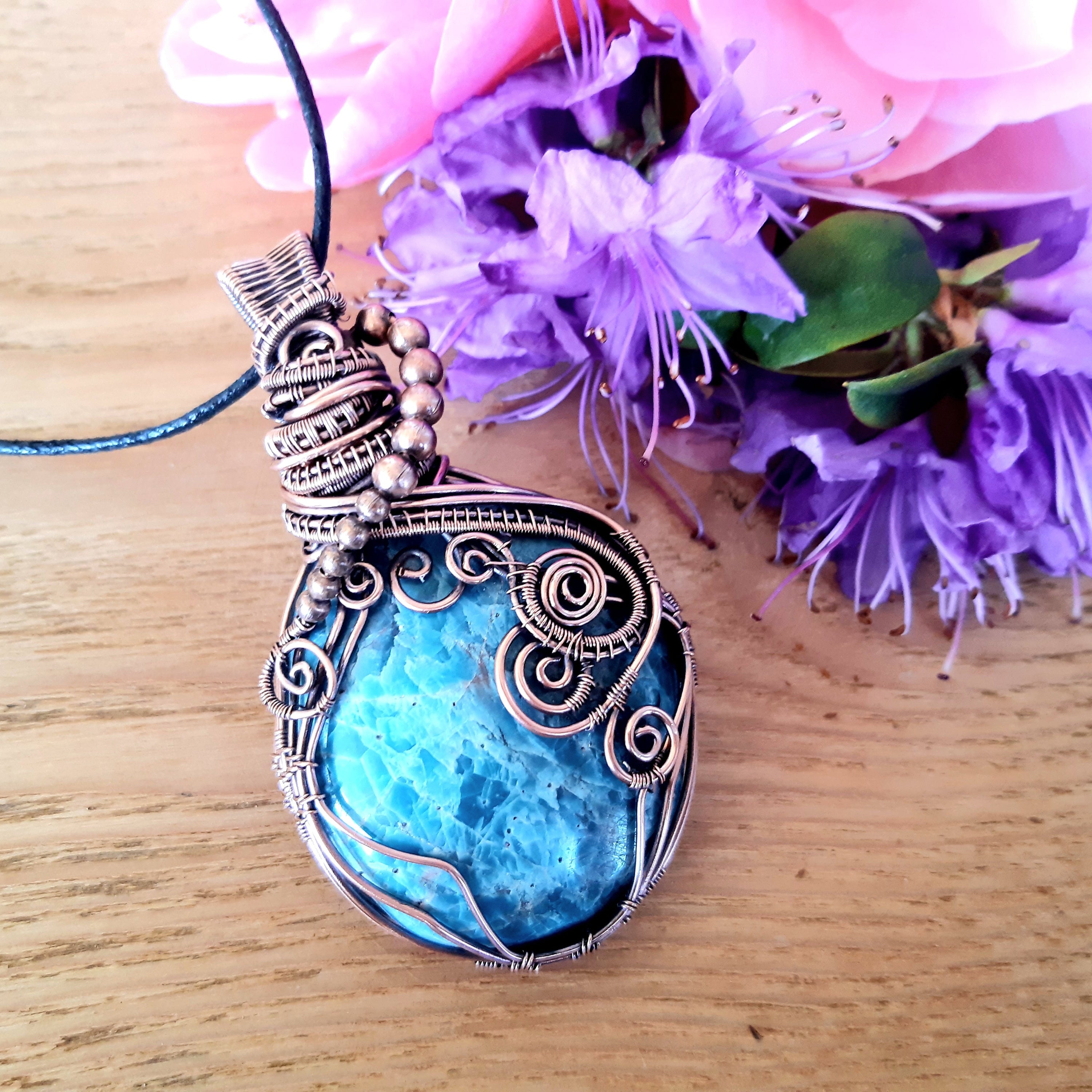 Blue pendant necklace on a wooden surface with purple flowers