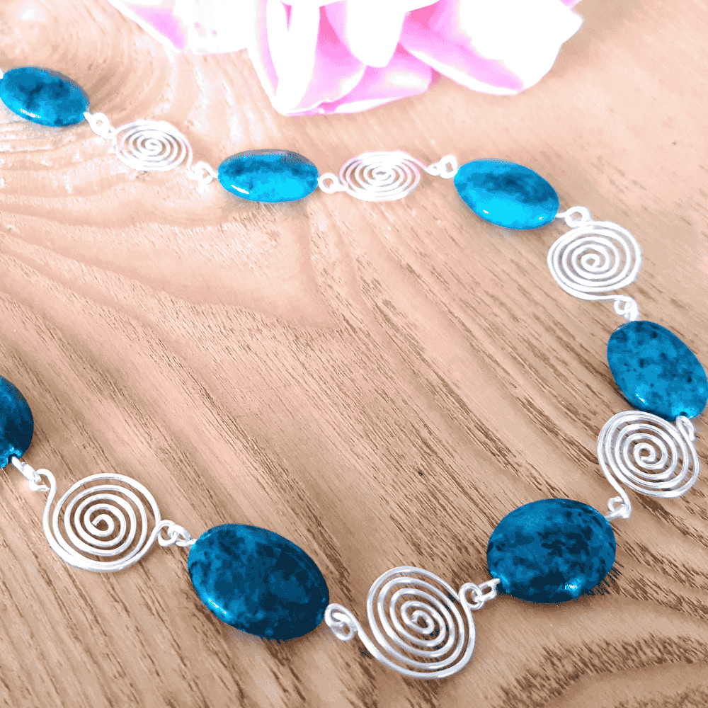 Necklace with blue beads and silver spiral designs on a wooden surface
