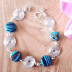 Bracelet with blue and black striped beads and silver circular links on a wooden surface