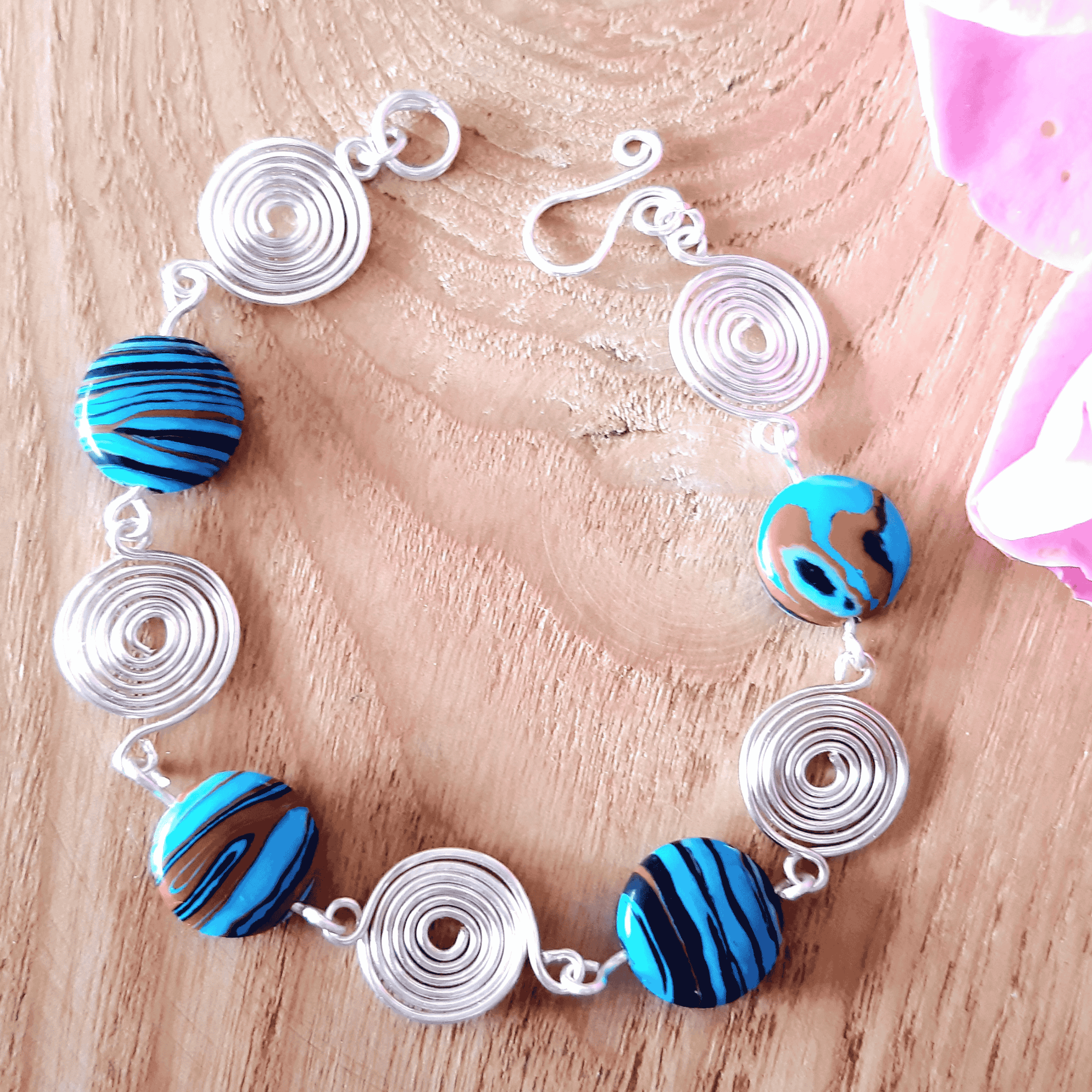 Bracelet with blue and black striped beads and silver circular links on a wooden surface