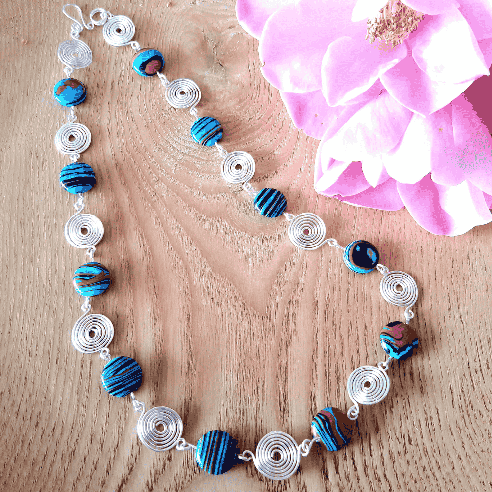 Necklace with blue and silver beads on a wooden surface with a pink flower.