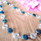 Necklace with blue and black circular beads  and silver spirals on a wooden surface with pink fabric in the background