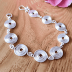 Detailed view of a closed silver spiral bracelet on a wooden surface