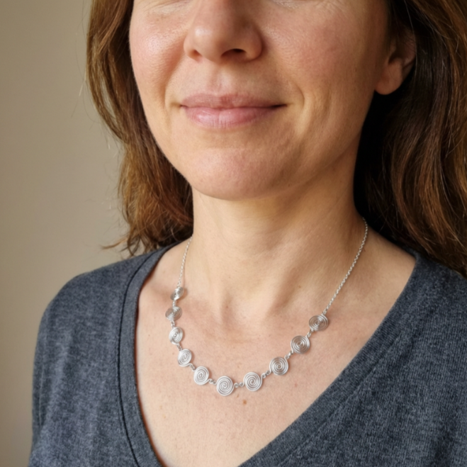 Woman wearing a silver necklace against a neutral background