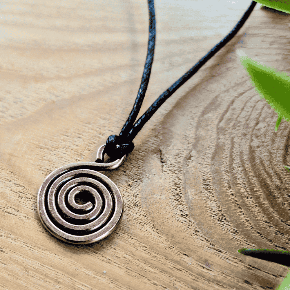 Copper spiral pendant on a black cord against a wooden background