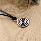Copper spiral pendant on a black cord against a wooden background