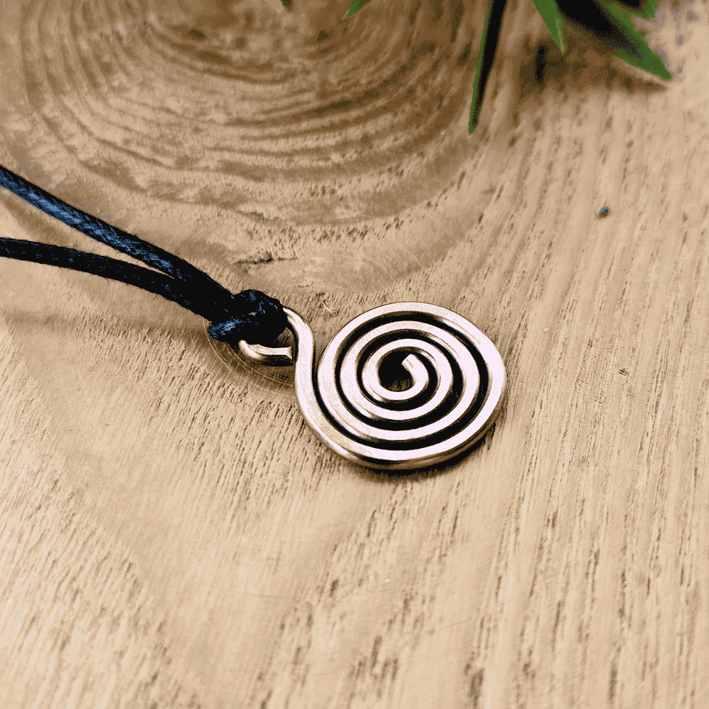 Copper spiral pendant on a black cord against a wooden background