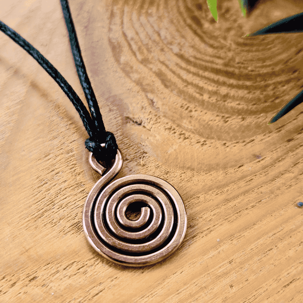 Copper spiral pendant on a black cord against a wooden background