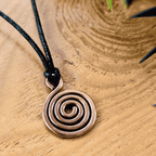Copper spiral pendant on a black cord against a wooden background