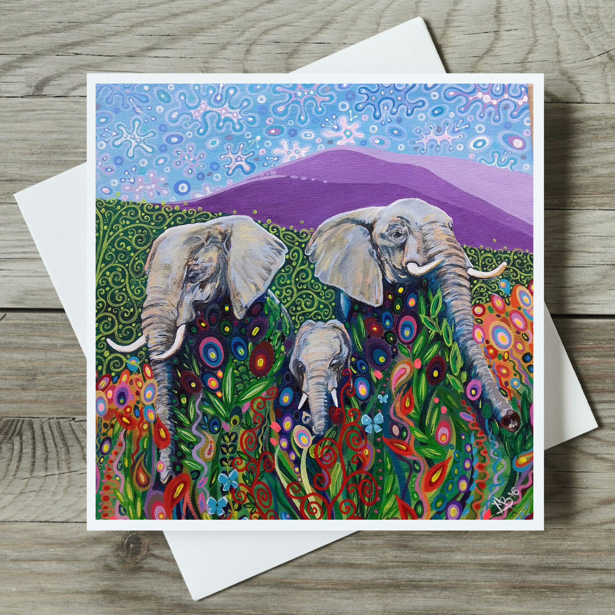 Colorful card with elephants and floral patterns on a wooden surface