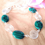 Bracelet with green beads and silver spiral designs on a wooden surface