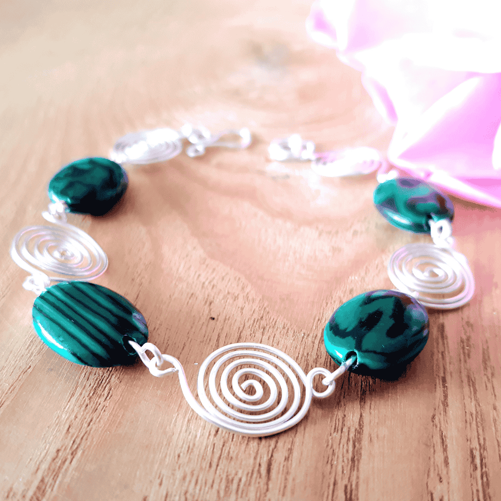 Bracelet with green beads and white spiral designs on a wooden surface