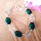 Bracelet with green beads and silver spiral designs on a wooden surface