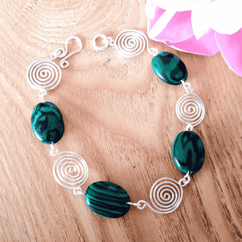 Bracelet with green beads and silver spiral designs on a wooden surface