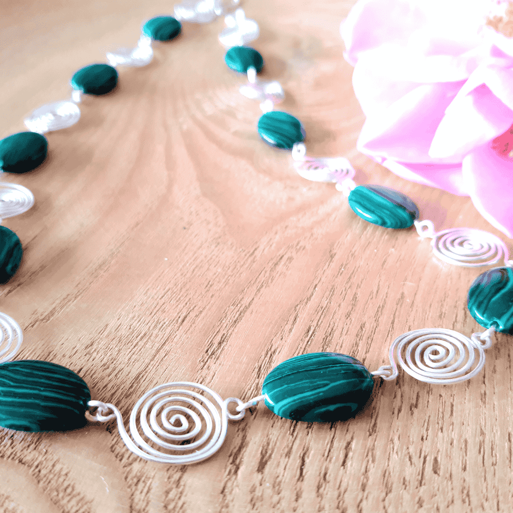 Necklace with green  beads and silver spirals on a wooden surface