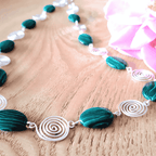 Necklace with green  beads and silver spirals on a wooden surface