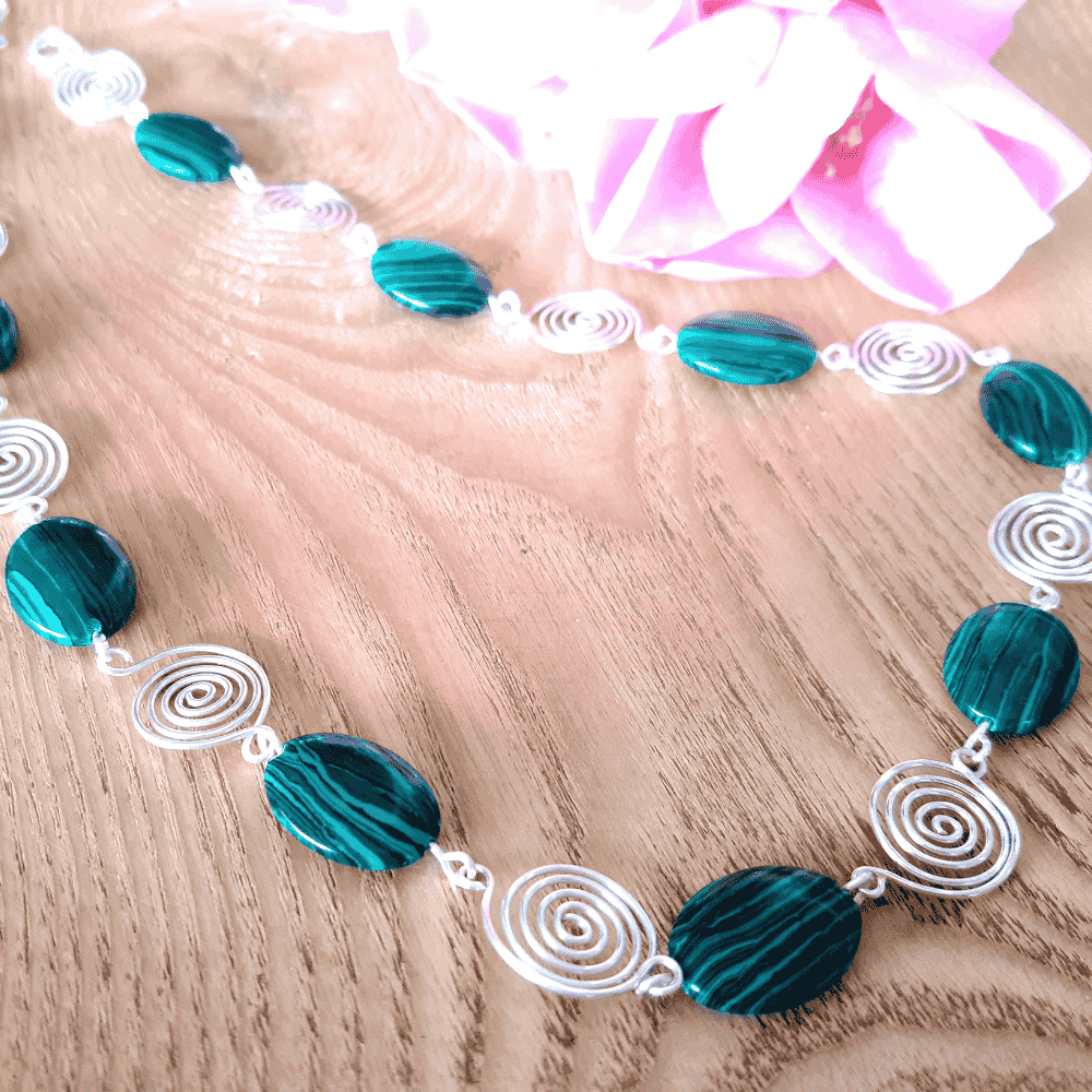 Necklace with green beads and silver wire patterns on a wooden surface