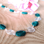 Necklace with green beads and silver spiral accents on a wooden surface