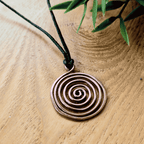 Bronze spiral pendant on a black cord with green leaves in the background